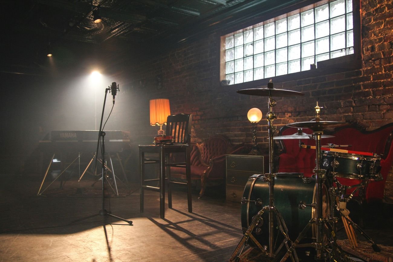 A rock and roll studio with a microphone, drum kit and lamps