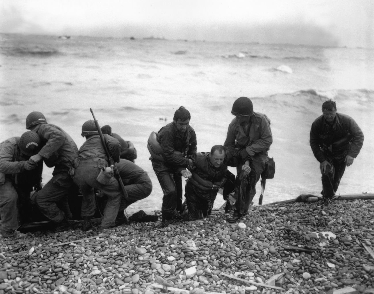 Soldiers helping men ashore on a stony beach, Normandy, June 1944